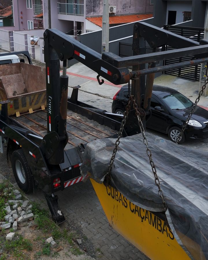 Caçamba amarela da Cubas Caçambas presa nas correntes do caminhão, sendo içada